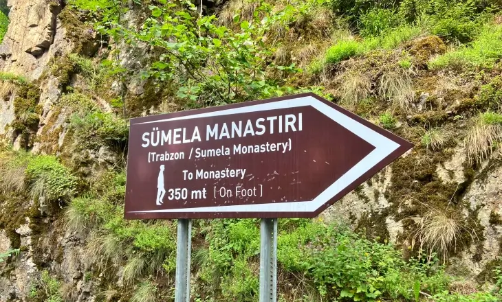 Sümela Manastırı yürüyüş yolu yön tabelası; 350 metre mesafe bilgisi ve yeşil ormanlık alan içinde konumu.